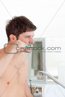 Good-looking young man brushing his teeth in the bathroom