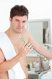 Positive young man with a towel brushing his teeth in the bathro
