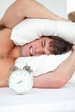 stressed man woken-up by his alarm clock putting his head under 