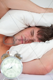 young male adult stressed by his alarm clock with his head under