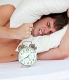 angry man stressed by his alarm clock lying on his bed