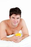 bare-chested man lying on his bed with a glass of orange juice