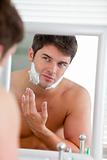 Young man putting some shaving foam looking his face in the mirror