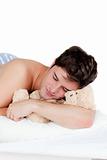 young man in pyjamas sleeping with a teddy-bear lying on his bed