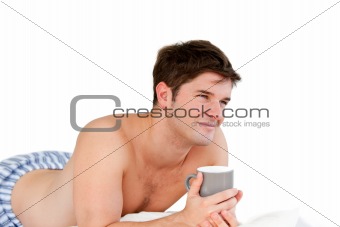 Smiling man holding a cup of coffee lying on his bed