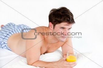handsome boy in pyjamas holding a glass of orange juice lying on