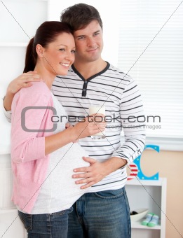 Portrait of a delighted pregnant woman holding a glass of milk and of her husband touching her belly