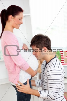 Portrait of a joyful man kissing his pregnant wife's belly