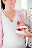 Close-up of a smiling pregnant woman eating strawberries and of her husband