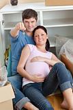 Happy couple expecting a baby sitting on the floor and holding t