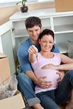 Delighted couple expecting a baby sitting on the floor and holdi