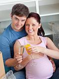 Happy couple expecting a baby drinking and sitting on the floor