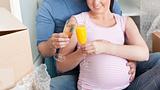 Smiling couple expecting a baby drinking and sitting on the floo