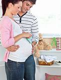 Smiling pregnant woman holding baby shoes while husband touching