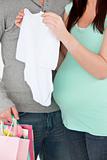 Close-up of a pregnant woman holding baby cloth and of her husband holding shopping bags