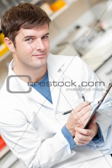 Handsome scientist holding a clipboard and smiling at the camera
