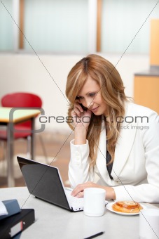 Busy businesswoman with laptop, coffee and food talking on phone