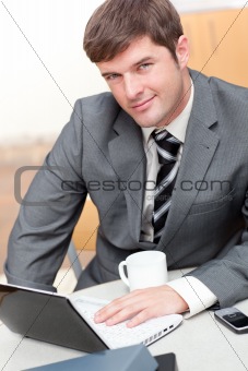Busy businessman with a laptop, a cellphone and a mug sitting at