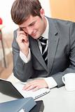 Assertive businessman talking on phone and using his laptop