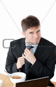 Elegant businessman having breakfast and touching his tie in fro