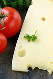 large piece of cheese varieties Maasdam  and tomato on cutting board