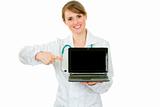 Smiling  medical doctor woman pointing finger on  laptop with blank screen
