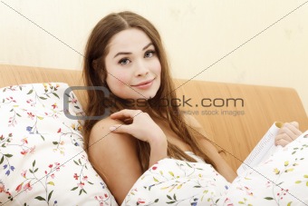 Beautiful woman reading a book while laying in a bed