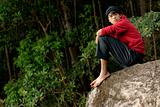 Asian man looking seated on rock outdoors
