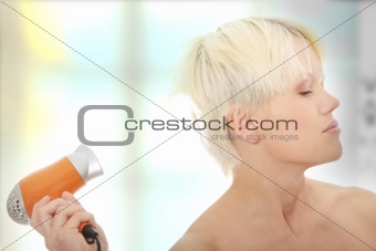 Young blonde woman using hair drier