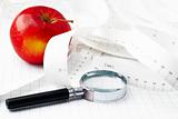 Red apple, measuring tape and magnifying glass on graph paper