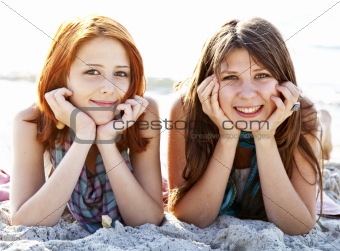 Two beautiful girls lie on the beach.