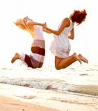 Two beautiful young girlfriends jumping on the beach