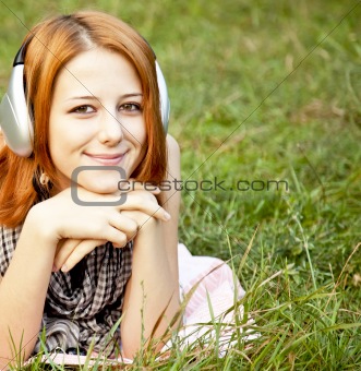 Young fashion girl with headphone lying at green grass