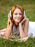 Young fashion girl with headphone lying at green grass at park. 