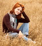 Beautiful red-haired girl at yellow autumn grass.