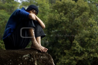 Troubled asian man sitting on rock outdoors