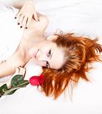 Beautiful red-haired girl with rose in the bedroom. 