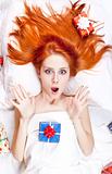 Surprised red-haired girl in bed with Christmas gifts.