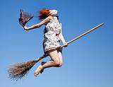 Young red-haired witch on broom flying in the sky