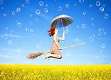 Red-haired girl fly with umbrella over rape field and bubbles 