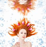 Beatiful red-haired girl with tulips in hair underwater.