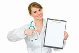 Smiling medical female doctor pointing finger on blank clipboard

