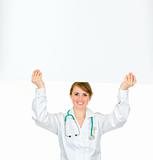 Smiling medical doctor woman holding blank billboard over her head
