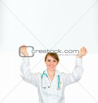 Smiling medical doctor woman holding blank billboard over her head
