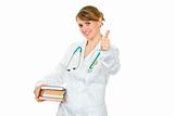Smiling young female doctor holding several books in hands
