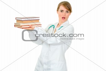 Shocked young female doctor holding several medical books in hands
