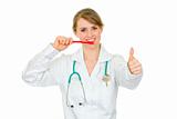 Smiling dentist female holding toothbrush and showing thumbs up gesture
