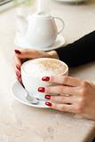 Morning cup of cappuccino and hand of a girl with red nails
