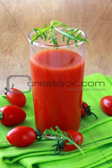 glass of tomato juice on the green cloth, with a cherry tomato