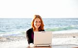 Portrait of red-haired girl with laptop at beach.